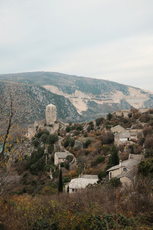 Panoramic view of Pocitelj Fortress old town with stone houses and medieval tower on a steep hillside above the river valley. Historic architecture blends with rugged landscape and muted autumn tonesの写真素材