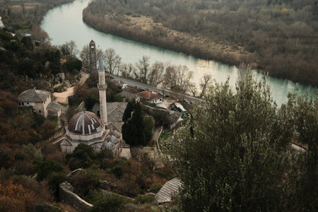 High angle view of Pocitelj village mosque and stone tower beside the Neretva River, surrounded by trees and historic buildings in a quiet Balkan landscapeの写真素材