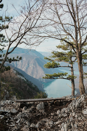 Wooden bench on rocky edge with view of Drina River and Perucac Lake framed by trees in Tara...