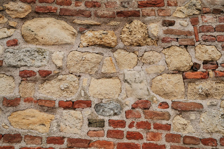 Close-up view of an old stone and brick wall with rough surface, showing weathered textures, natural...