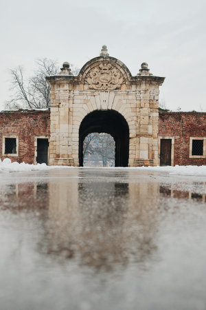 Historic stone fortress gate in winter with snow and wet pavement, showcasing medieval architecture, symmetry, and entrance to an old defensive complexの写真素材
