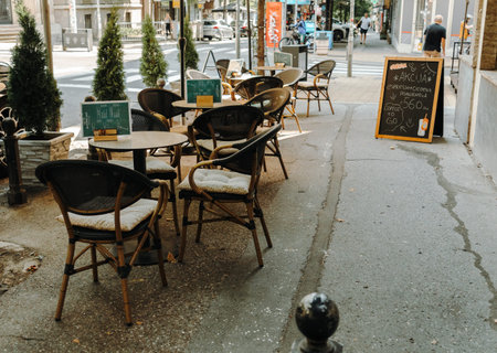Belgrade, Serbia - July 23, 2026. Empty tables and chairs line a shaded sidewalk cafe terrace in the city center