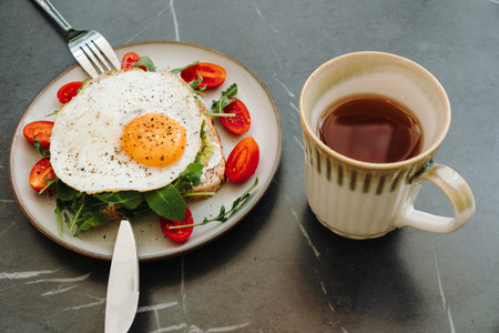 Avocado toast topped with a fried egg served with a cup of hot tea. Fresh vegetables complete a balanced breakfast