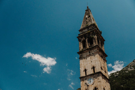 Close view of the historic clock tower of Saint Nicholas Church in Perast under a clear blue sky. Landmark architecture overlooking Boka Bay in Montenegro