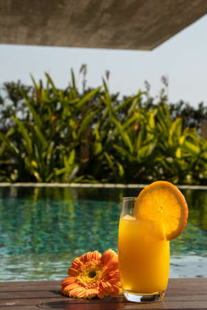 orange juice, served by the pool, healthy breakfast, as orange juice with flower beside the crystal clear pool with clear water on a sunny dayの写真素材