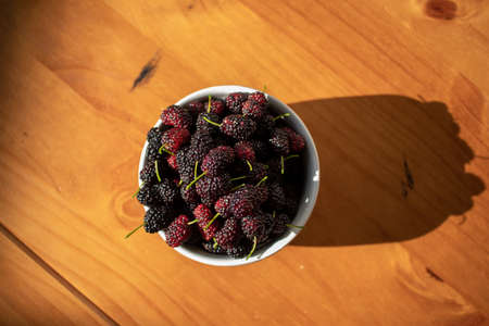 Fresh blueberry in a bowl on the table for healthy breakfast, white bowl with fresh blueberries on the wooden table with morning sun illuminating the scene.の写真素材