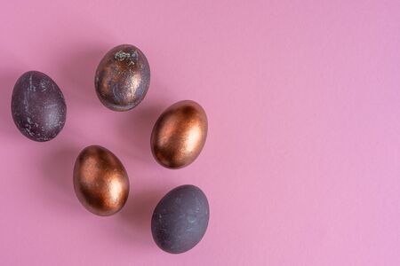 Colored painted pearl chicken eggs of violet, golden color on pink background. Minimalistic creative ideaの写真素材