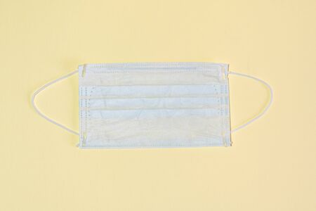 Protective medical mask on a yellow background flat lay top view.
