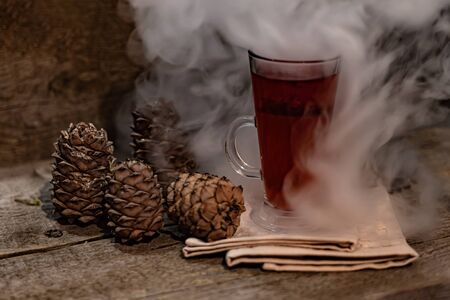 Glass of red tea in a spectacular smoke and pine cones on a wooden backgroundの写真素材
