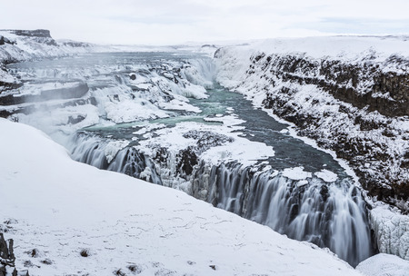 Majestic Gullfoss waterfalls form a half frozen triangle as the Hvita River falls into a wintry...
