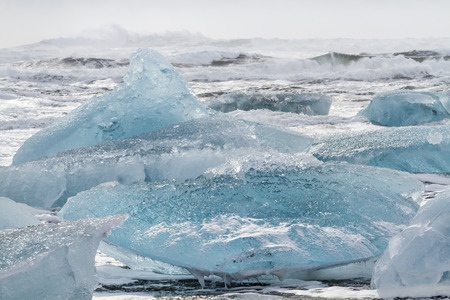 Large blue semi-trasnparent icebergs in the crashing surf on the black sand beach at Jokulsarlon in...