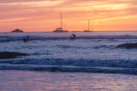 Surfers silhouetted against a brilliantly colored sunset  