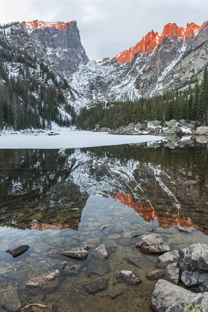 Hallett Peak and Flattop Mountain glow pink at sunrise, reflected in Dream Lake in Rocky Mountain National Park.の写真素材