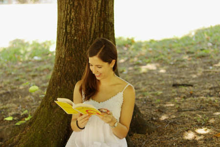 Girl with white dress sitting on a tree with a bookの写真素材