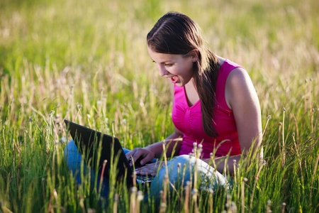 pretty , young woman using her laptop computer outdoors in the middle of a lovely field - staring at the screen in amazementの写真素材
