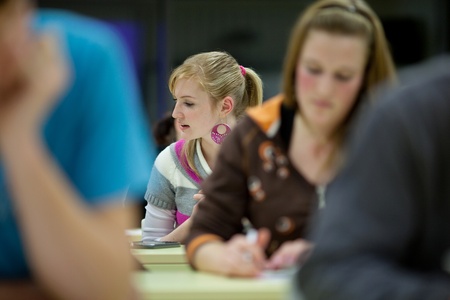 pretty female college student sitting in a classroom full of students during class (shallow DOF; color toned image)の写真素材