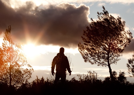 facing the dusk - young man's silhouette against dramatic sky with clouds and late evening sunshine の写真素材