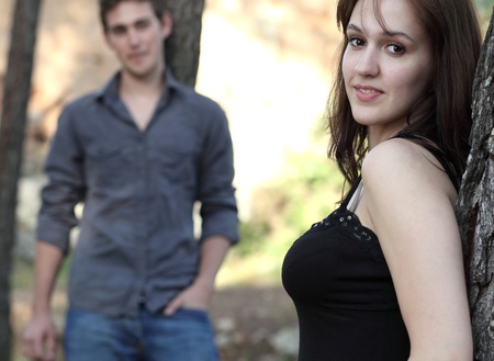Beautiful young couple outdoors in a park - looking at the camera (focus on the young woman)