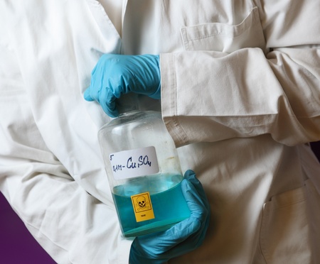 male scientist wearing protective gloves holding a toxic blue chemical in front of a violet wall の写真素材