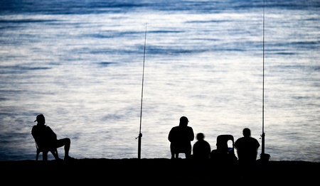 Sea/Ocean fishing - fishermen sitting by the sea/ocean in darkness waiting for the catchの写真素材