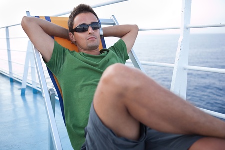 Young man resting on a deckchair while traveling on a liner across a sea/oceanの写真素材