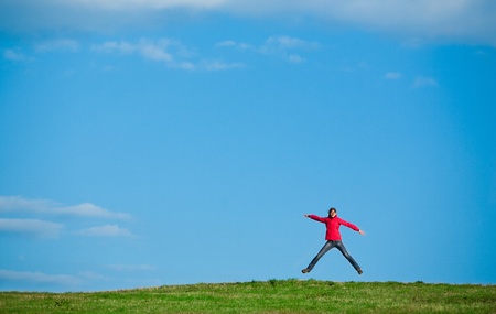joyful young woman jumping in the midlle of a green field