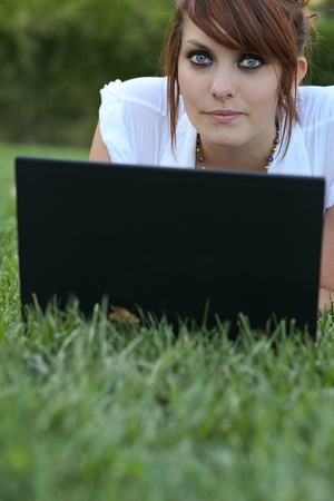 Pretty young woman lying on the grass - using her laptop computerの写真素材