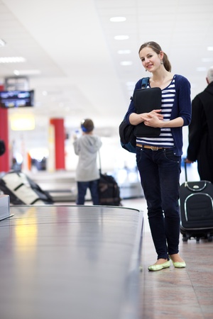 Baggage reclaim at the airport - pretty young woman taking her suitcase off the baggage carousel の写真素材