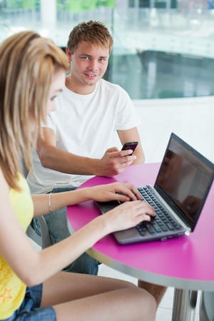 two college students having fun studying together, using a computer in a university library/study room (shallow DOF, color toned image)の写真素材