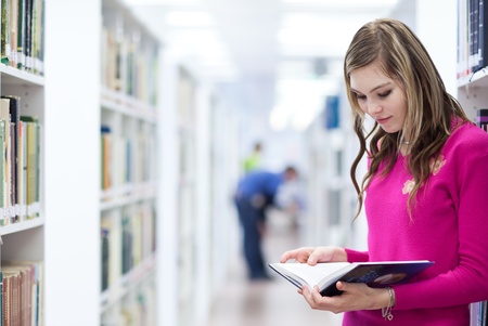 in the library - pretty, female student with laptop and books working in a high school library (color toned image)の写真素材