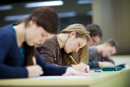 pretty female college student sitting in a classroom full of students during class pretty female college student sitting in a classroom full of students during class