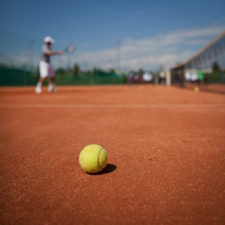 Tennis player in action on tennis court (selective focus, focus on ball in the foreground)の写真素材