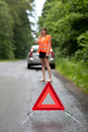 Young female driver wearing a high visibility vest, calling the roadside service/assistance after...