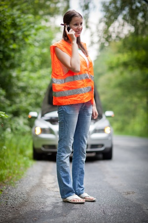 Young female driver wearing a high visibility vest, calling the roadside service/assistance after her car has broken downの写真素材