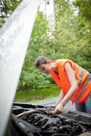 Young female driver wearing a high visibility vest, checking the engine after her car has broken downの写真素材