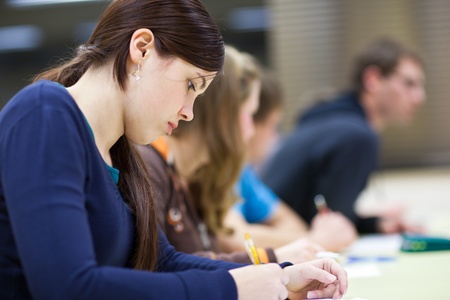 pretty female college student sitting in a classroom full of students during class (shallow DOF; color toned image)の写真素材