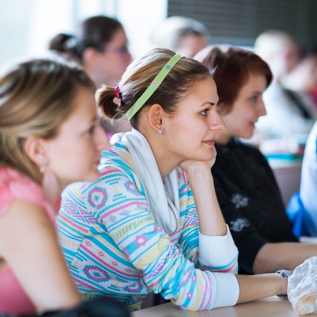 young, pretty female college student sitting in a classroom full of students during class (shallow DOF; color toned image)の写真素材