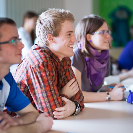 young, handsome college student sitting in a classroom full of students during classの写真素材