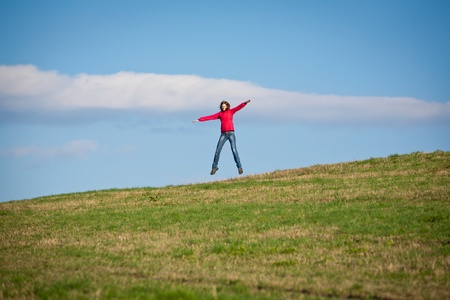 Young woman jumping for joy against blue sky in the middle of a green field