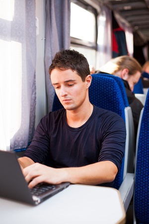 Handsome young man using his laptop computer while on the train (shallow DOF; color toned image)の写真素材