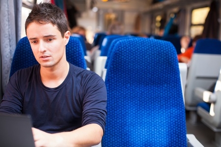 Handsome young man using his laptop computer while on the train (shallow DOF; color toned image)の写真素材