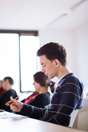 young, handsome male college student sitting in a classroom full of students during class (color toned image; shallow DOF)の写真素材