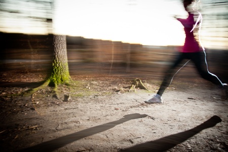 Young woman running outdoors in a city park on a cold fall/winter day (motion blurred image)の写真素材