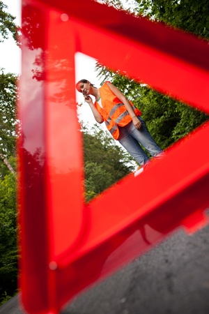 Young female driver wearing a high visibility vest, calling the roadside service/assistance after her car has broken downの写真素材