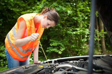 Young female driver wearing a high visibility vest, bending over the engine of her broken down carの写真素材