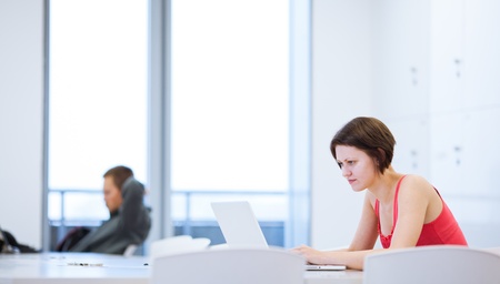 Pretty young college student studying in the library/a study room at campus (shallow DOF)の写真素材