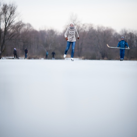 Young woman ice skating outdoors on a pond on a freezing winter day