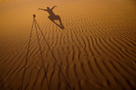 Shadow of a photographer levitating next to his tripod cast on dunes of sand in a desertの写真素材
