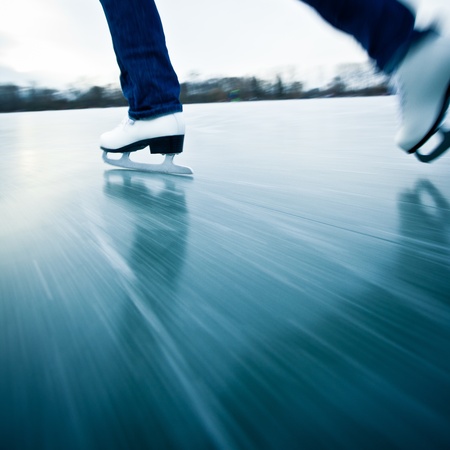 Young woman ice skating outdoors on a pond on a freezing winter day - detail of the legs (motion blur is used to convey speed)の写真素材