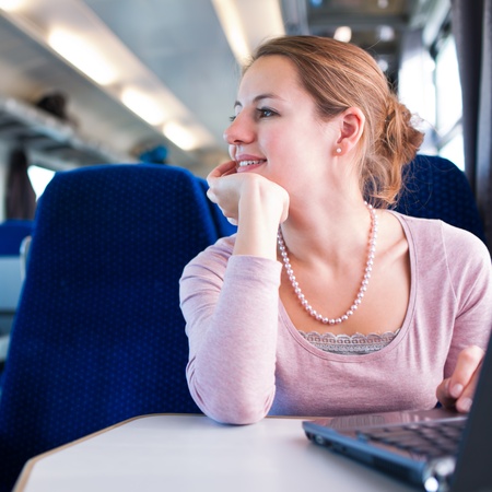 Young woman using her laptop computer while on the train (shallow DOF; color toned image)